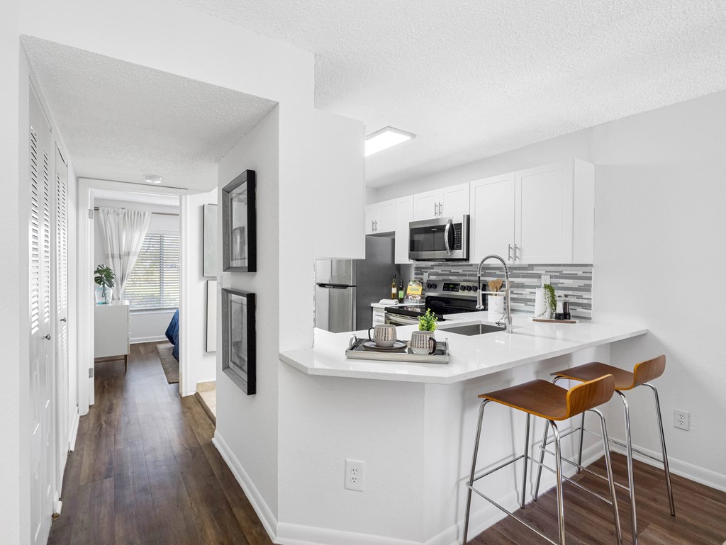 A kitchen with white cabinets and a white island with brown stools.